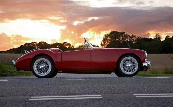 Beautiful red old cabriolet with white tires on the road against a cloudy sky