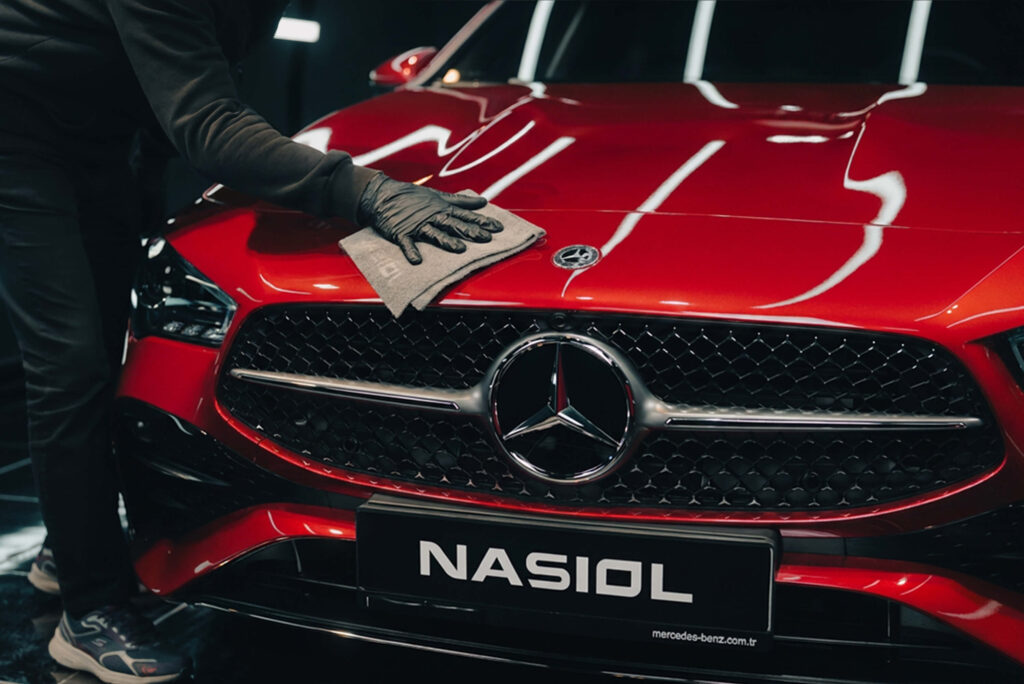 Person in black gloves wiping the hood of a red Mercedes-Benz with a microfiber cloth in a workshop