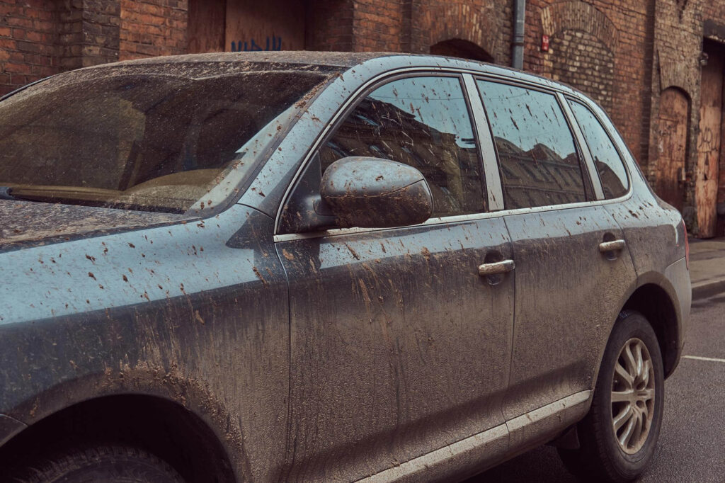 Blue SUV covered in mud parked beside a brick wall outside.